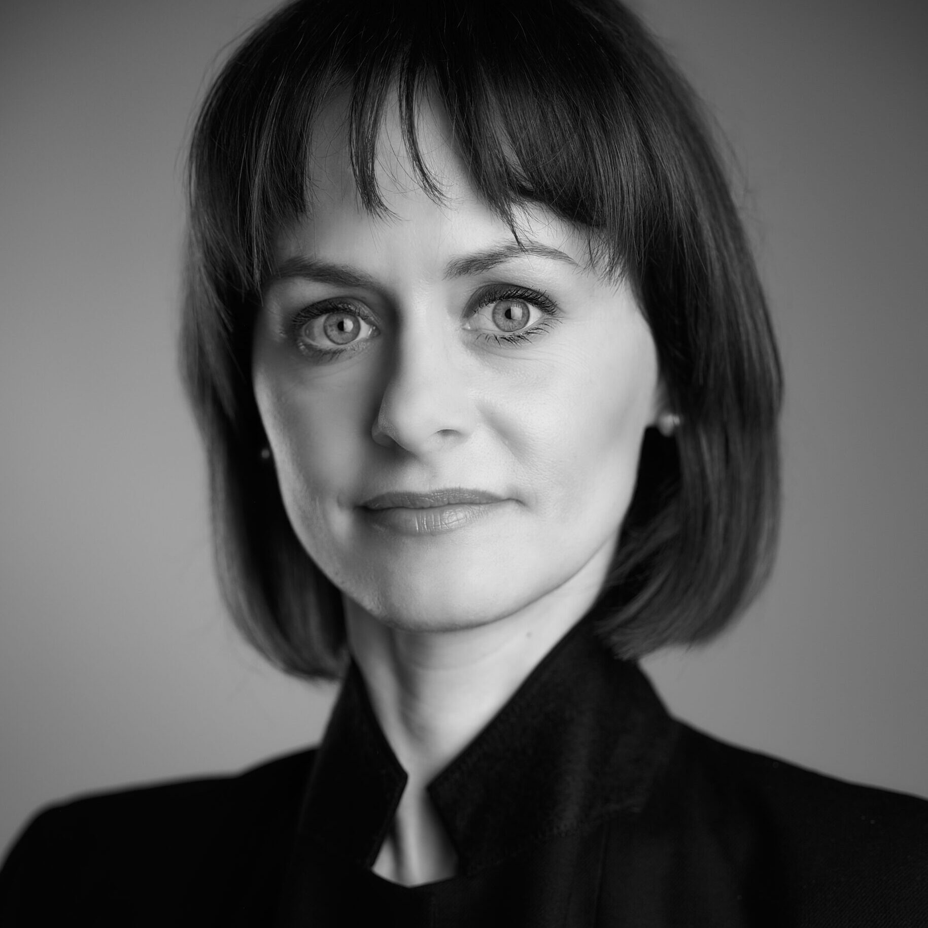 Czarno-białe zdjęcie. Popiersie kobiety o ciemnych półdługich włosach z grzywką. Ubrana w czarną koszulę ze stójką.