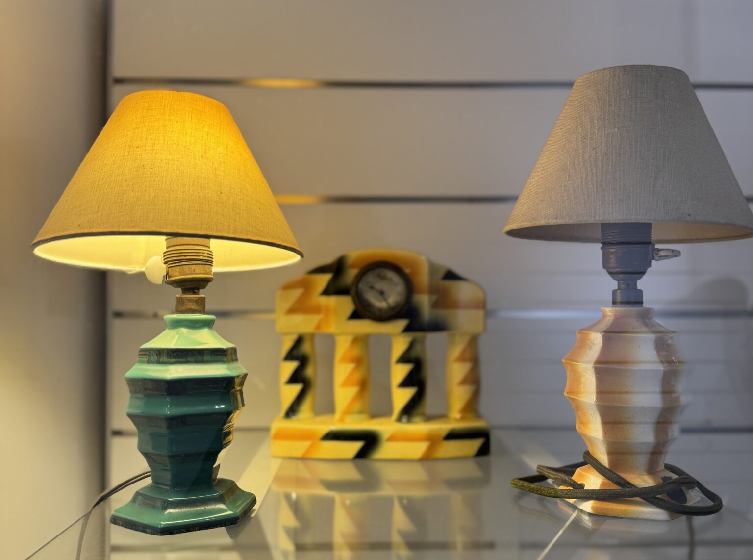 Dwie lampki z abażurami, między nimi w tle zegar. Mają kanciaste formy i ekspresyjne zdobienia.