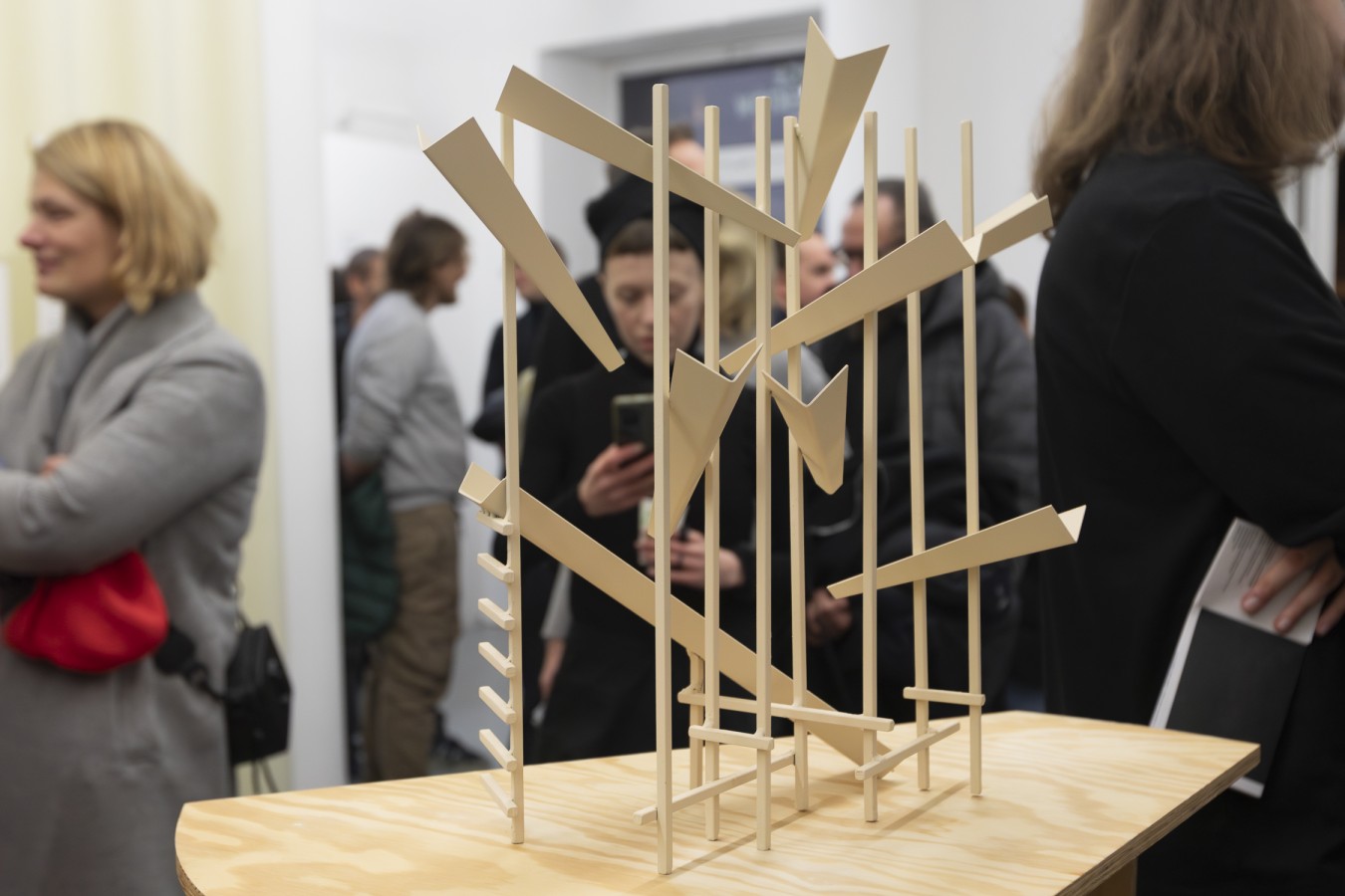 Wnętrze galerii. Na pierwszym planie rzeźba - delikatna konstrukcja z pionowych i ukośnych listewek. W tle za rzeźbą grupa zwiedzających.